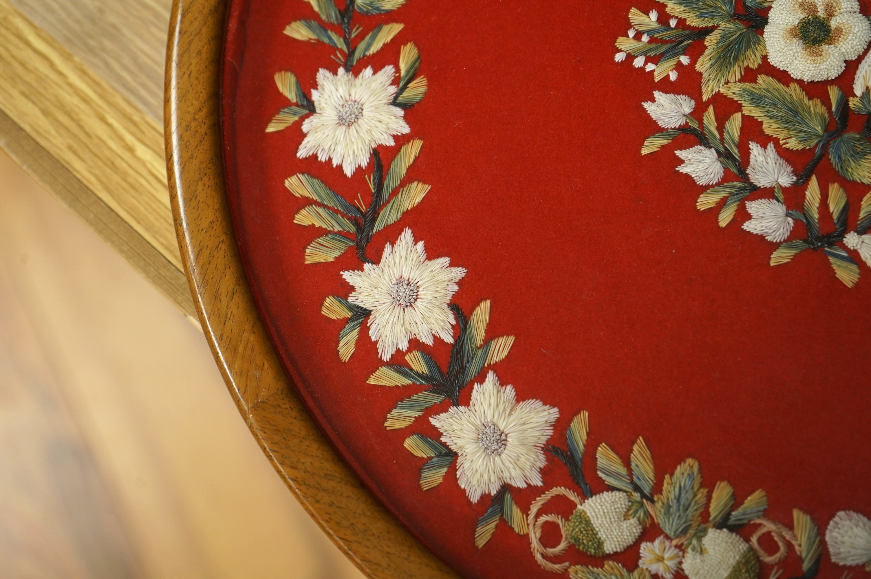 A framed, 19th century, possibly Scandinavian, red felt circular multi-coloured silk embroidery of flowers, acorns and leaves, also embroidered with fine stump work style beadwork flower detail, 32cm diameter. Condition